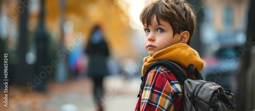 Reluctant schoolboy with backpack unwilling to leave mom, encouraged by her. photo