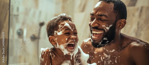 Happy African father and son enjoying playful moment with shaving foam in bathroom. photo