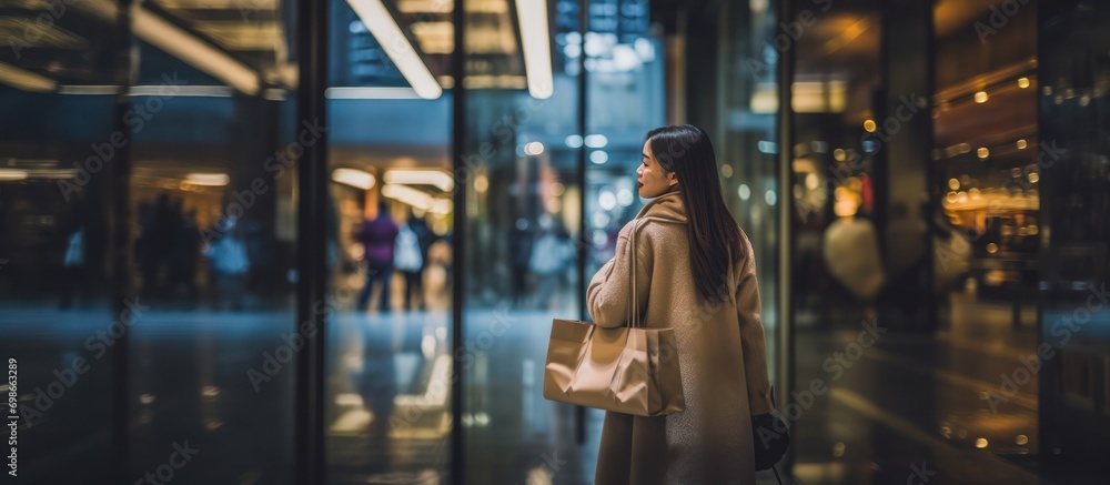 Rear view of happy young Asian woman carrying paper bag and coat shopping center background in mall