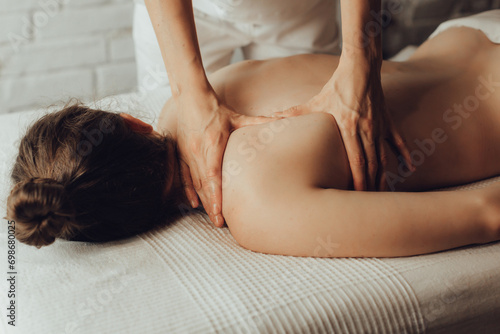 Obraz na plátně Hands of female chiropractor massaging shoulders of young woman lying on massage table