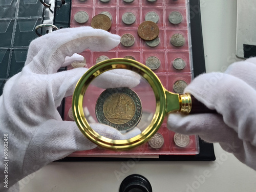 Woman numismatist examining coin with magnifier photo