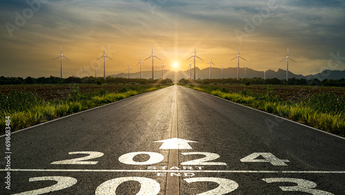 Word 2024 written on the road in the middle of asphalt road to wind generators at sunset.Concept of New year 2024,ESG,clean energy,eco energy,planning,challenge,business strategy,opportunity,change photo