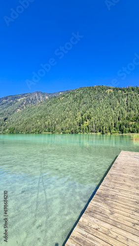 Wooden platform at east bank of alpine lake Weissensee in Carinthia, Austria. Wooden pier in turquoise water of bathing lake. Remote untouched nature in summer. Vacation vibes. Remote forest on hills photo