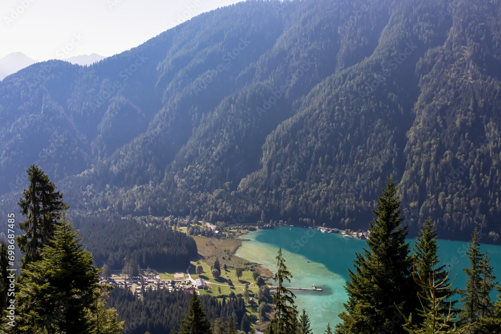 Aerial view of east bank of alpine lake Weissensee in Carinthia, Austria. Pristine turquoise water of bathing lake. Tranquil forest in serene landscape in remote untouched nature in summer. Vacation