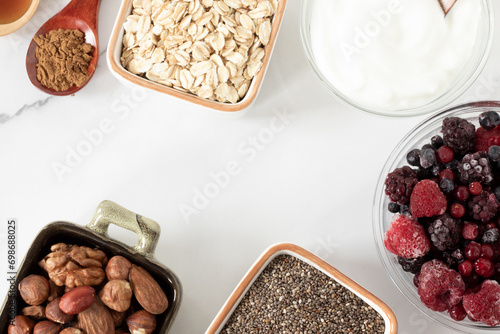Healthy organic fiber food ingredients for breakfast preparation. Frozen fruit, nuts, chia seeds, cinnamon, and Greek yogurt on white. Top view.