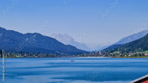 Scenic view of east bank of alpine lake Weissensee in Gailtal Alps, Carinthia, Austria. Bathing lake surrounded by mountain ranges of Austrian Alps. Serene landscape amidst untouched nature in summer