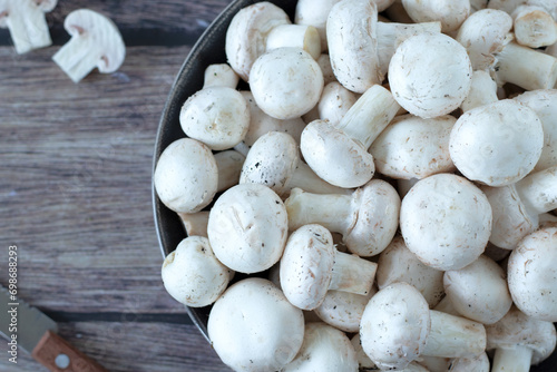 White button champignon mushrooms (agaricus bisporus) in a bowl with knife on wooden table. Top view, close-up.