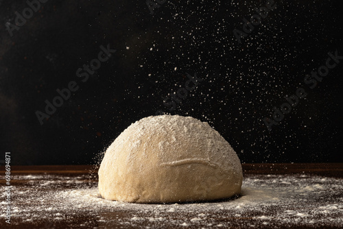 Wallpaper Mural Pastry chef sprinkles flour on fresh raw dough for bread or pizza on a dark background. Torontodigital.ca