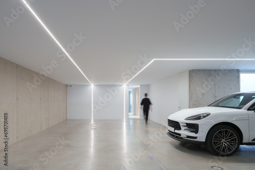 Unrecognizable person walking in contemporary garage with integrated LED lighting, polished concrete floor, and a parked luxury car photo