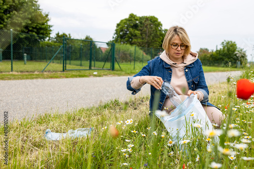 Adult woman kneeling with a garbage bag collecting plastic waste for recycling