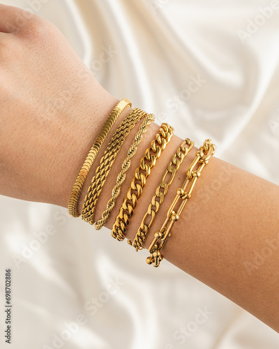 Girl wearing set of gold chain bracelets on wrist with silky fabric background