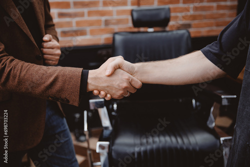 Happy Barber greeting male client in barbershop, warm toning photo