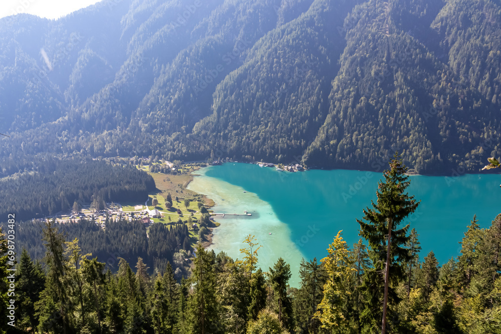 Aerial view of east bank of alpine lake Weissensee in Carinthia, Austria. Pristine turquoise water of bathing lake. Tranquil forest in serene landscape in remote untouched nature in summer. Vacation