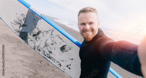 Canvas Print Extreme selfie photo Surfer man in wetsuit with surfboard, winter surfing in ocean, sunlight
