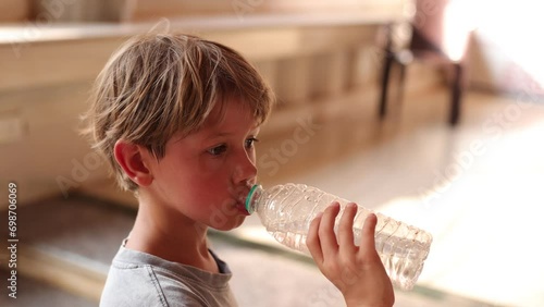 Cute 6-7-year-old boy in enjoys drinking water from plastic bottle indoors. Active games . 