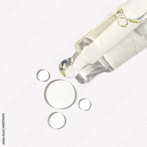 Clear serum in glass dropper with texture drops on white background