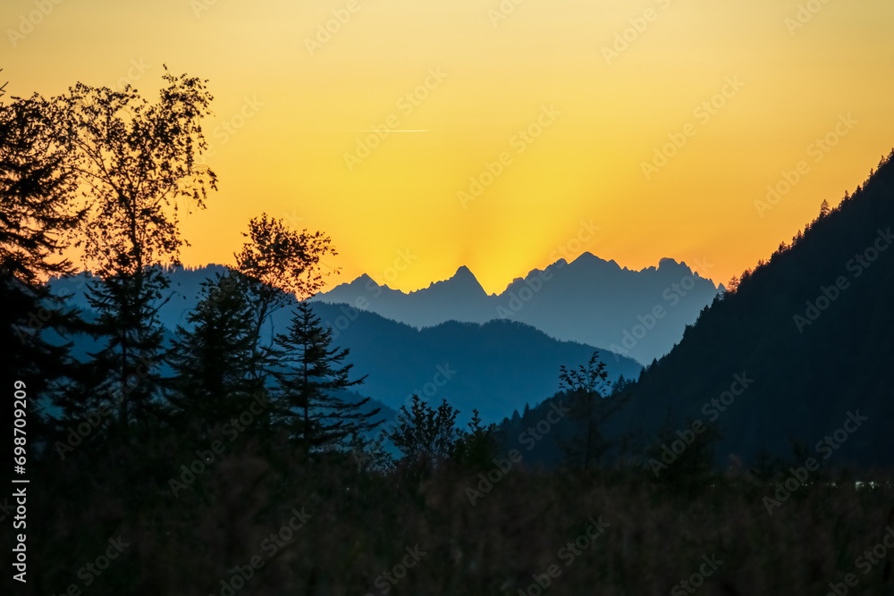 Silhouette of majestic mountain peaks against backdrop of vibrant sunset. Panoramic viewing point at east bank of Weissensee in Carinthia, Austria. Gazing through tranquil forest, romantic atmosphere