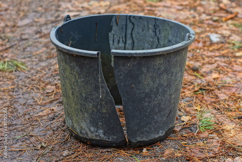 one plastic black dirty broken discarded industrial without a handle empty round bucket stands on the ground during the day on the street