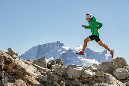 Runner in a green jacket leaping between rocks in high altitude photo