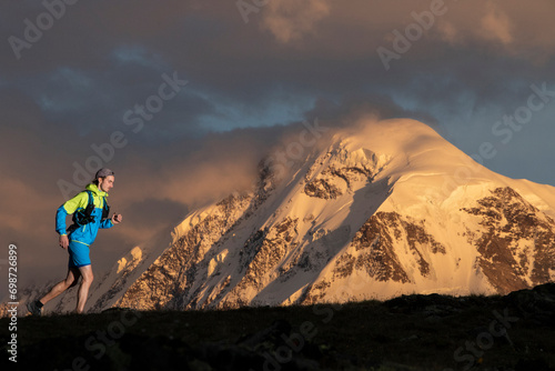 Trail runner before majestic snowy mountain at sunset photo