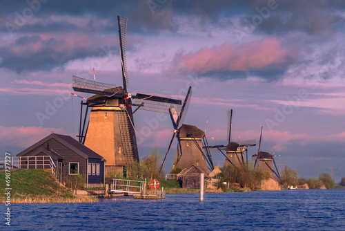 Sunset over a serene Dutch landscape with a row of historic windmills and waterfront houses at Kinderdijk