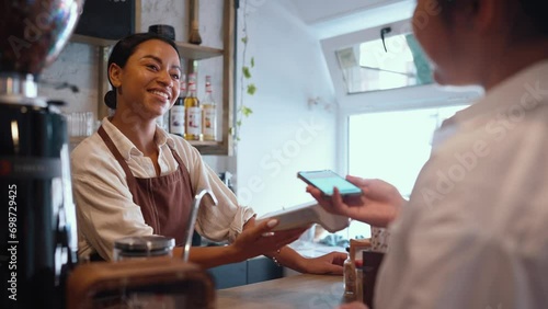 Smiling african female barista accepting bank card payments through terminal behind counter at cafe