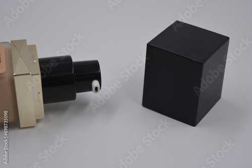 Beautiful, stylish women's cosmetics, very cool glass bottle with foundation, foundation and black matte black square black cap arranged on a white plastic background. photo