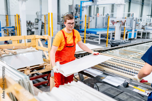 Conveyor production of large sheets of cut glass. Male warehouse worker portrait in warehouse storage.