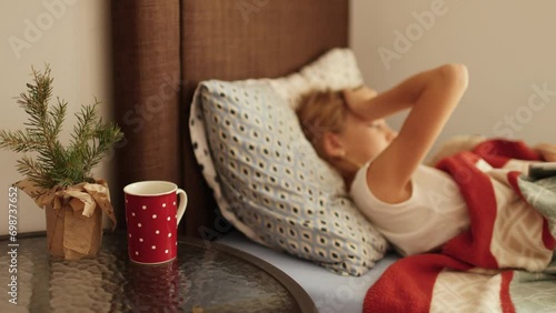Sick little girl in bed on Christmas, focus on red dotted cup with hot tea on a table near child's bed