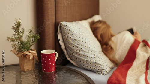 Unhealthy sick ill little girl lying in bed at home turned away blurry silhouette, focus on table with red cup