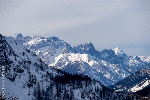 Panoramic view on snow capped mountain peaks of Karawanks and Julian Alps in Carinthia, Austria. Looking at summits Mangart and Montasio. Remote alpine landscape in Baerental. Mystical cloudy sky
