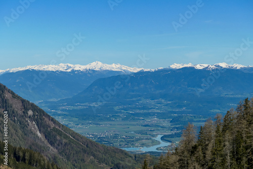 Scenic view on Sinacher Gupf in Karawanks mountains and the Drava river in Rosental valley in Carinthia, Austria. Forest in early spring. Snow capped Hohe Tauern mountain range can be seen. Sunny day © Chris