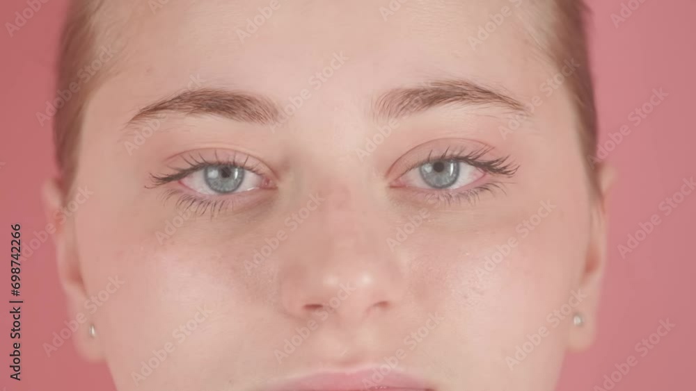 In the close up shot on a pink background, a young, attractive girl is depicted. She is supposedly underwater, staring at the camera and blinking. At this time, the water send wave blurring its image In the close up shot on a pink background, a young, attractive girl is depicted. She is supposedly underwater, staring at the camera and blinking. At this time, the water send wave blurring its image