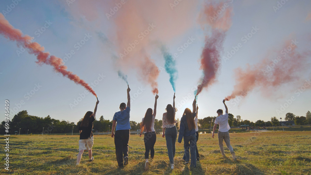 A group of friends spraying multi-colored smoke at sunset. - obrazy, fototapety, plakaty 