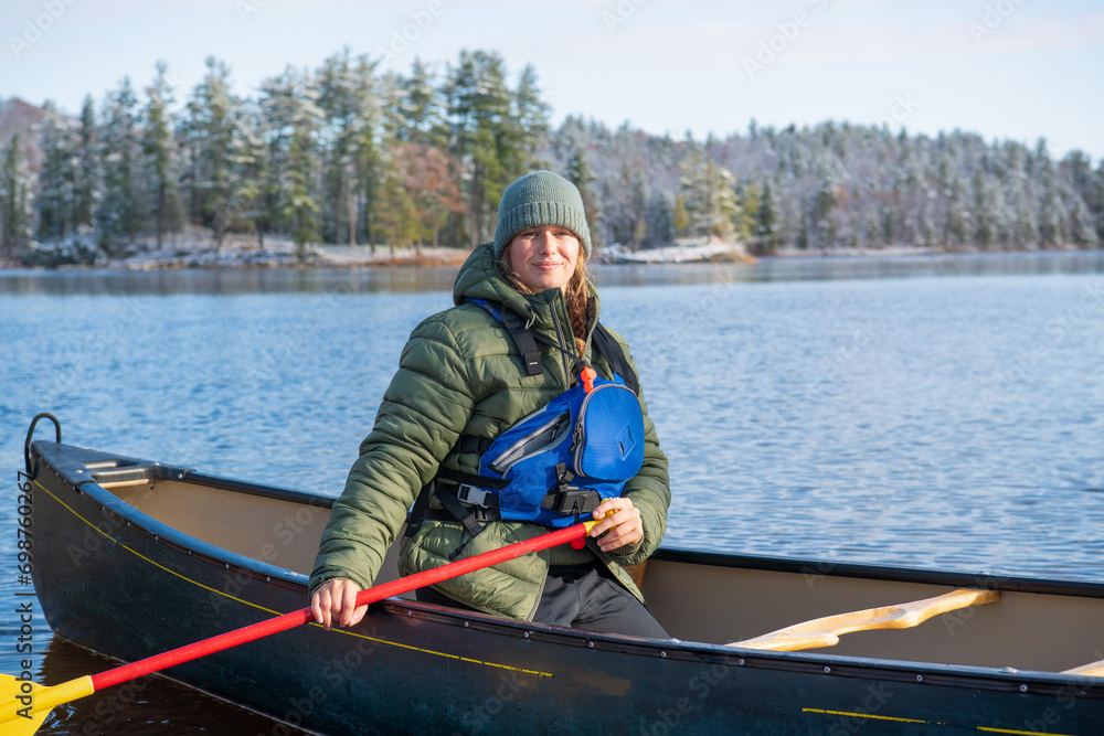 young woman paddling a green canoe solo on a river with trees clad in freshly fallen snow in the background room for text shot on the ottawa river in eastern ontario canada	
