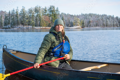 young woman paddling a green canoe solo on a river with trees clad in freshly fallen snow in the background room for text shot on the ottawa river in eastern ontario canada 