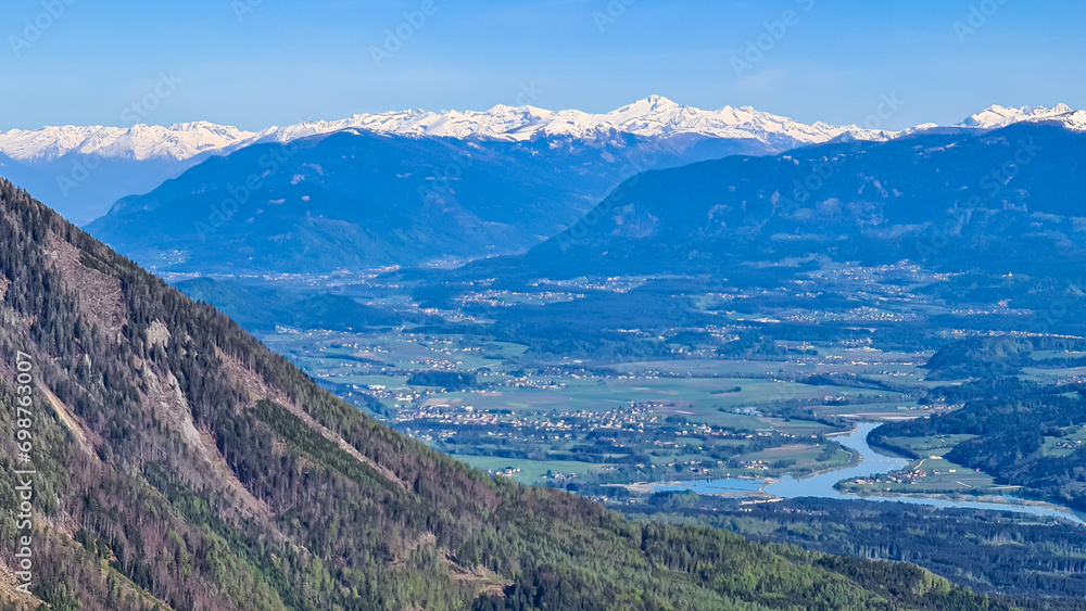 Scenic view on the Drava river in Rosental valley on the way to Kosmatitza in Carinthia, Austria. Forest in early spring. The Hohe Tauern mountain range can be seen in the back. Sunny day. Hike