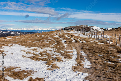 Front view of woman with hiking backpack on snow covered alpine meadow walking along fence from Ladinger Spitz to Gertrusk, Saualpe, Lavanttal Alps, Carinthia, Austria, Europe. Trekking early spring photo
