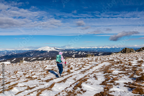 Woman with hiking backpack walking on snow covered alpine meadow on trail from Ladinger Spitz to Geierkogel, Saualpe, Lavanttal Alps, Carinthia, Austria. Snow capped mountain ranges of Austrian Alps photo