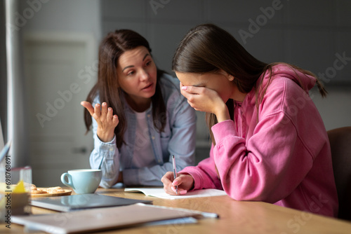 Angry mother scolding teen daughter for bad school results at home, mom arguing disciplining child must study. Parent and children conflicts concept photo