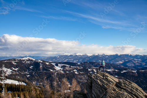 Woman with backpack standing on massive rock formation at Steinerne Hochzeit, Saualpe, Lavanttal Alps, border Styria Carinthia, Austria, Europe. Panorama of alpine meadows and snowcapped mountains photo