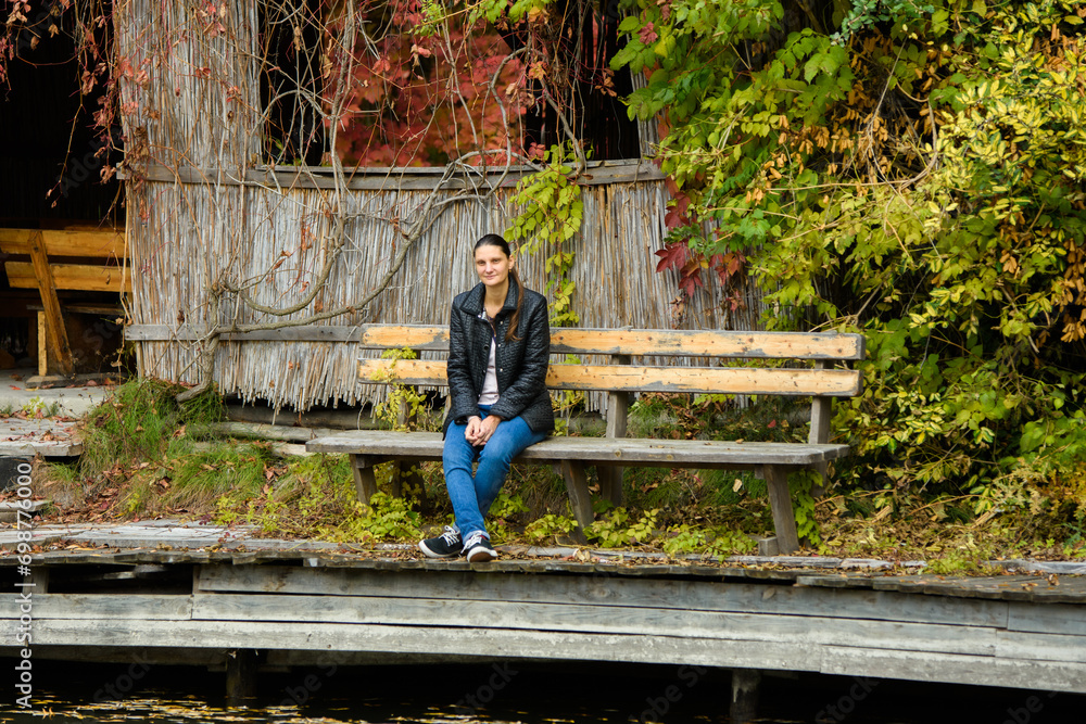 A young beautiful girl in casual clothes sits on a bench in an autumn park