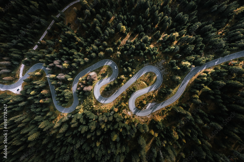 Car driving on a serpentine road leading through Italian Dolomites in autumn colors. Curvy road surrounded by pine forest.