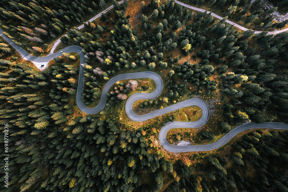 Car driving on a serpentine road leading through Italian Dolomites in autumn colors. Curvy road surrounded by pine forest.