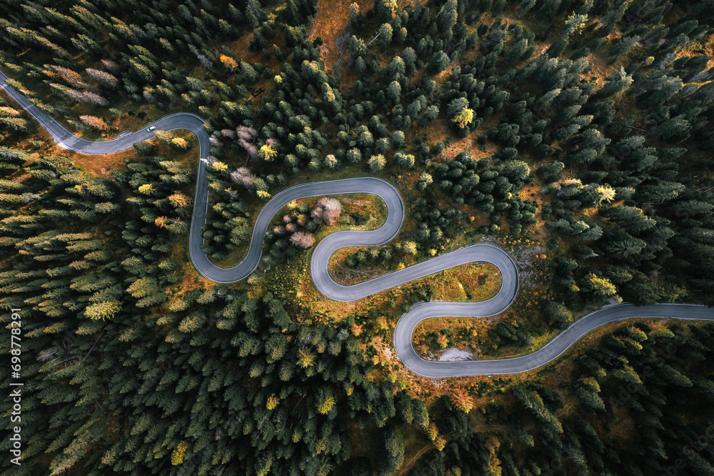Car driving on a serpentine road leading through Italian Dolomites in autumn colors. Curvy road surrounded by pine forest.