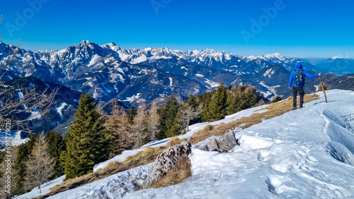 Man on panoramic hiking trail on way to snow covered mountain peak Ferlacher Horn in Carinthia, Austria. Alpine landscape of Austrian Alps. Wanderlust in tranquil serene nature. Winter wonderland photo