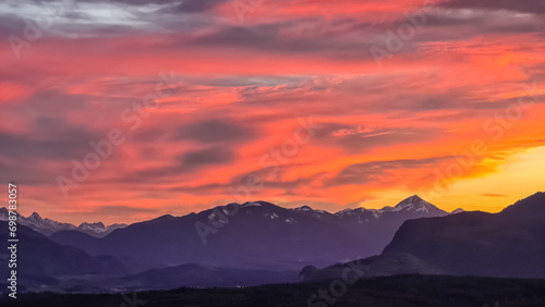 Scenic view of snow capped mountain peak Dobratsch at sunset seen from Taborhoehe in Carinthia  Austria  Europe. Sky has vibrant orange and pink colors with clouds swirling around summit. Serenity