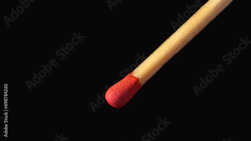 A macro shot of a matchstick against a black background. A wooden match with red sulfur.