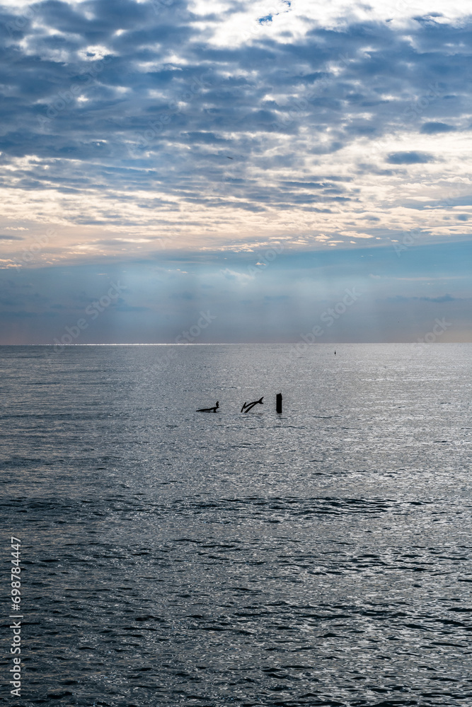 Obraz premium Grado, Italy - November 19th, 2023: View of the sea from the dam. Magical beams of light that start from the clouds and create a suggestive atmosphere. Filtering light on a sunny day.