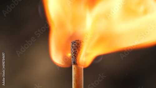 Macro shot of a burning match against a dark studio background. The flame of the burning match illuminates the dark space. The burning match is enveloped in an orange, vibrant and dynamic flame. photo